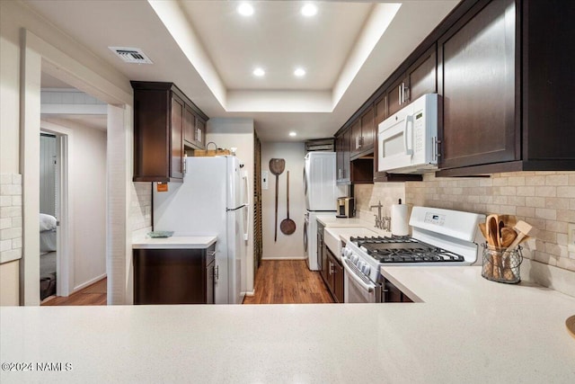 kitchen featuring white appliances, dark brown cabinets, a tray ceiling, and decorative backsplash