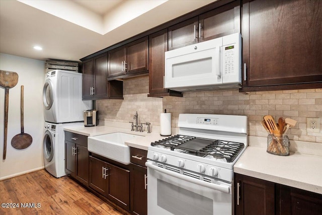 kitchen with sink, stacked washer and clothes dryer, white appliances, dark brown cabinetry, and light wood-type flooring