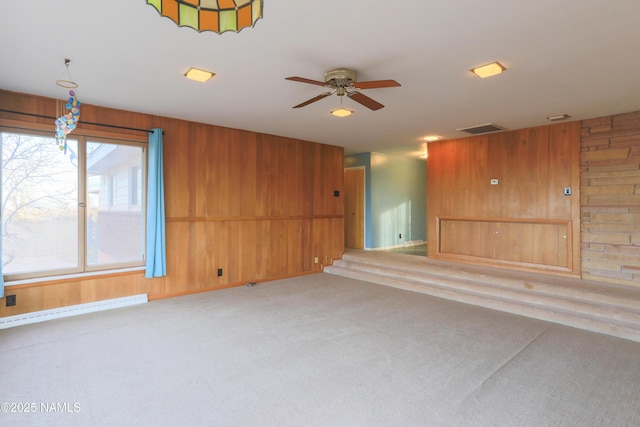 carpeted empty room featuring wooden walls and ceiling fan