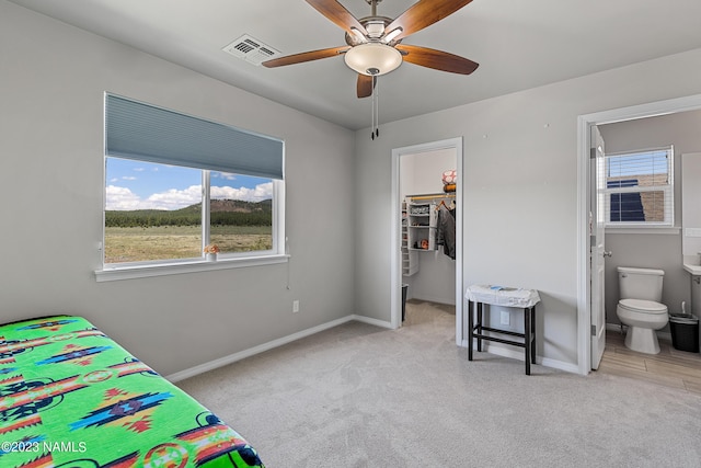 bedroom with light carpet, ceiling fan, a walk in closet, connected bathroom, and a closet