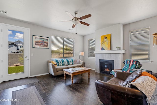 living room featuring a tile fireplace, dark wood-type flooring, and ceiling fan