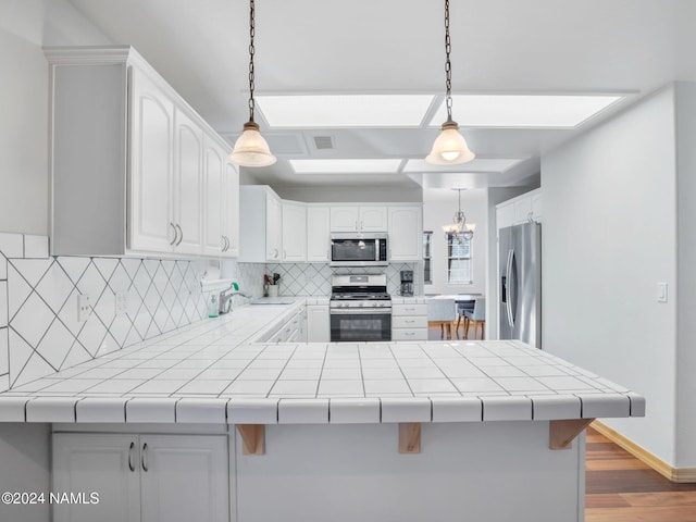 kitchen with tile counters, backsplash, appliances with stainless steel finishes, and kitchen peninsula