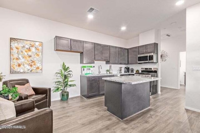 kitchen with light hardwood / wood-style floors, dark brown cabinets, stainless steel appliances, and a kitchen island