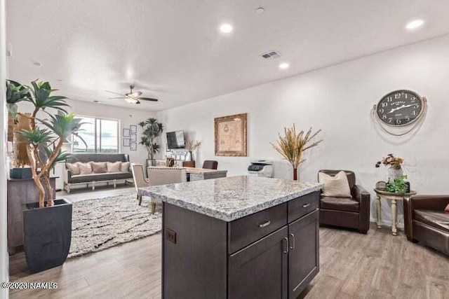 kitchen featuring light stone countertops, dark brown cabinetry, a kitchen island, light wood-type flooring, and ceiling fan