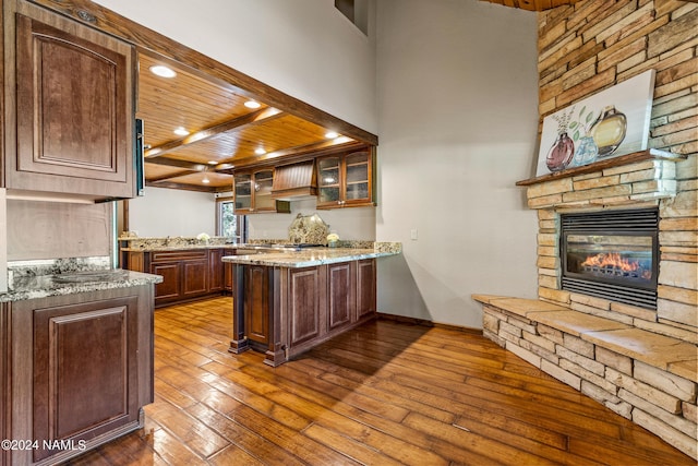 kitchen featuring hardwood / wood-style floors, wooden ceiling, a fireplace, kitchen peninsula, and light stone counters