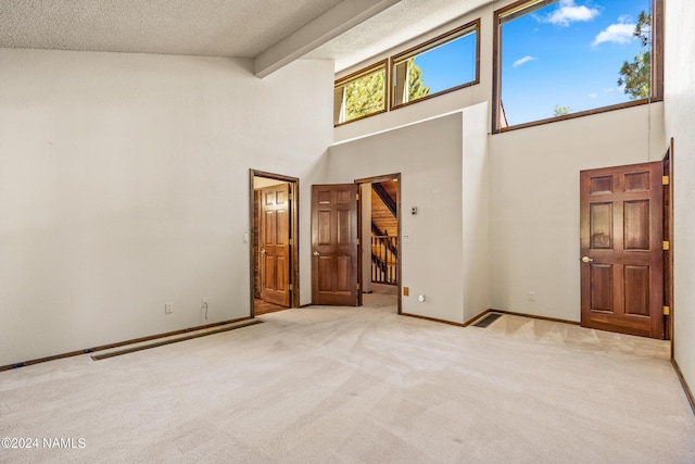 carpeted empty room with a towering ceiling, beam ceiling, and a textured ceiling