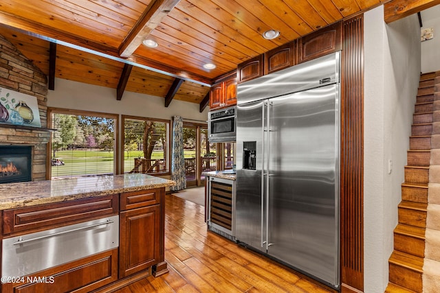 kitchen featuring wine cooler, stainless steel built in refrigerator, a stone fireplace, light stone countertops, and wooden ceiling