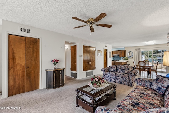 living room featuring ceiling fan, light colored carpet, and a textured ceiling