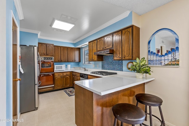 kitchen with appliances with stainless steel finishes, tasteful backsplash, a kitchen breakfast bar, sink, and kitchen peninsula