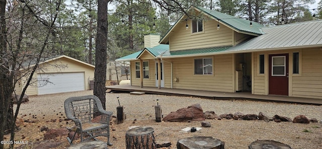 view of front of house with a porch, a detached garage, an outbuilding, metal roof, and a chimney