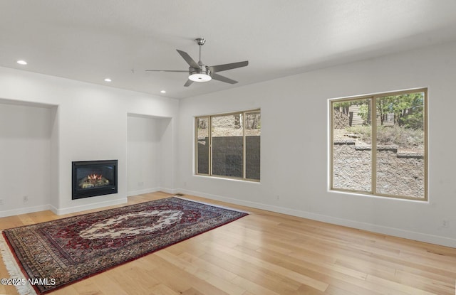 living area featuring ceiling fan, light wood-style flooring, recessed lighting, baseboards, and a glass covered fireplace