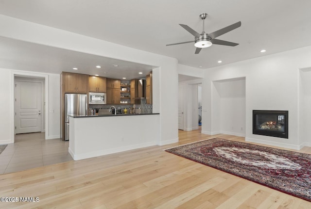 living area featuring a glass covered fireplace, baseboards, light wood finished floors, and recessed lighting