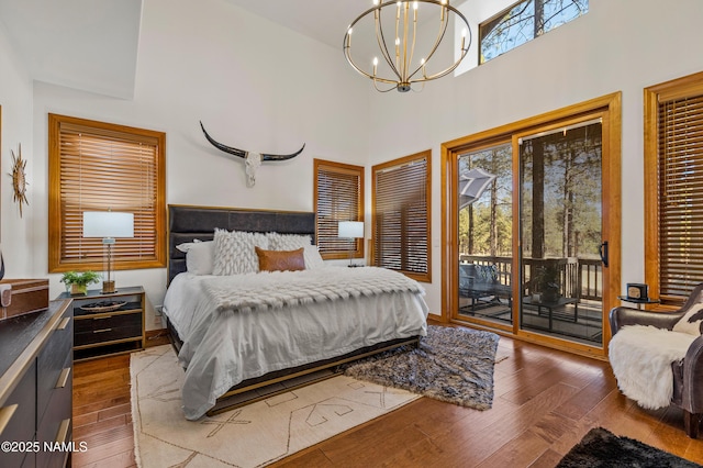 bedroom featuring dark wood-type flooring, a chandelier, multiple windows, and access to outside