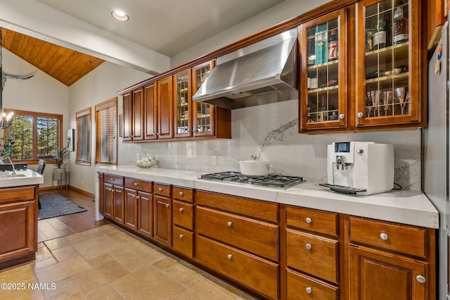 kitchen featuring vaulted ceiling with beams, tasteful backsplash, wooden ceiling, stainless steel gas stovetop, and wall chimney range hood