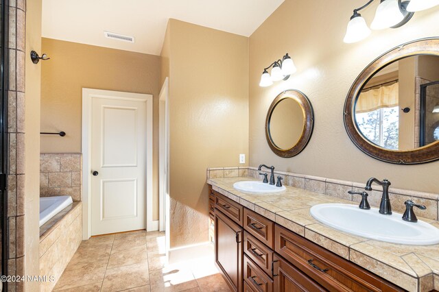 bathroom featuring tile patterned floors, a relaxing tiled tub, and vanity