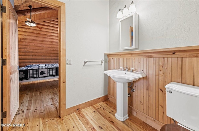 bathroom with toilet, log walls, and hardwood / wood-style floors