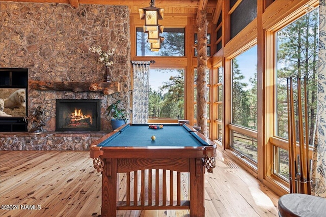 rec room featuring a stone fireplace, beam ceiling, light hardwood / wood-style floors, and pool table