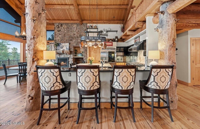 kitchen with stainless steel built in fridge, ventilation hood, kitchen peninsula, light wood-type flooring, and beam ceiling