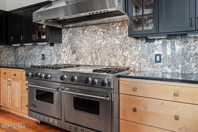 kitchen featuring wall chimney range hood, light brown cabinets, range with two ovens, backsplash, and hardwood / wood-style flooring