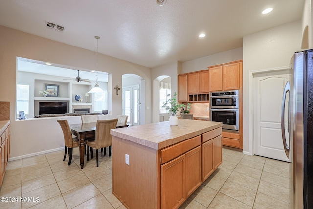 kitchen with a center island, stainless steel appliances, hanging light fixtures, light tile patterned flooring, and a tile fireplace