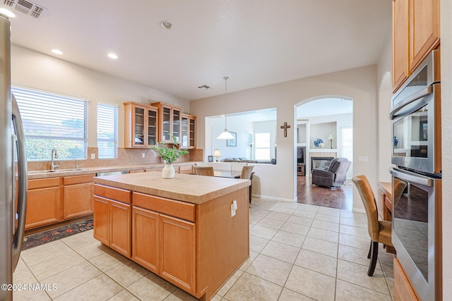 kitchen featuring decorative light fixtures, sink, light tile patterned flooring, a center island, and stainless steel appliances