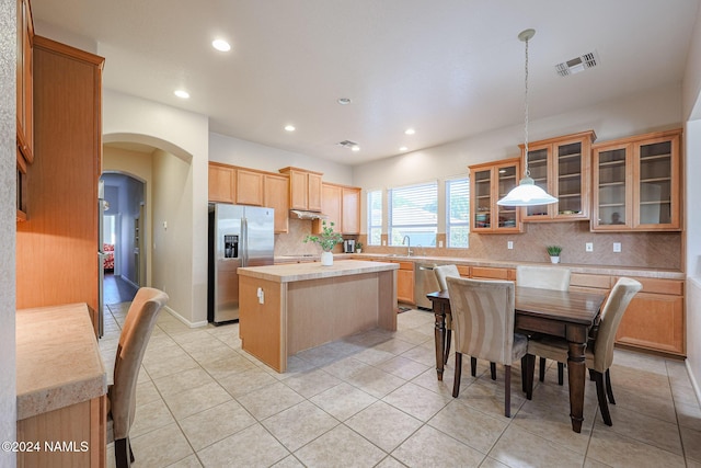 kitchen with pendant lighting, a kitchen island, stainless steel appliances, backsplash, and light tile patterned floors