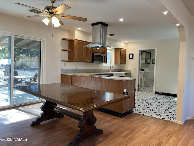 kitchen with light hardwood / wood-style flooring, ceiling fan, independent washer and dryer, island exhaust hood, and kitchen peninsula