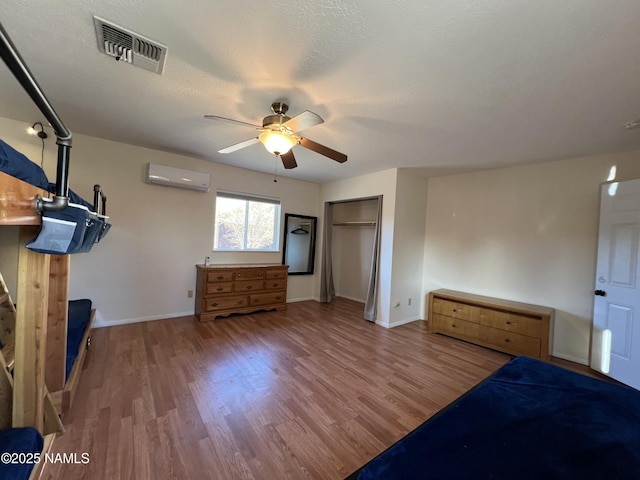 unfurnished bedroom featuring wood-type flooring, a wall mounted air conditioner, a textured ceiling, a closet, and ceiling fan