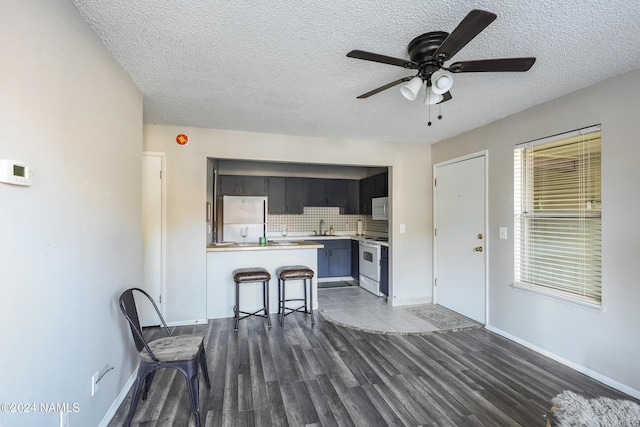 kitchen featuring white appliances, a textured ceiling, sink, kitchen peninsula, and a breakfast bar area