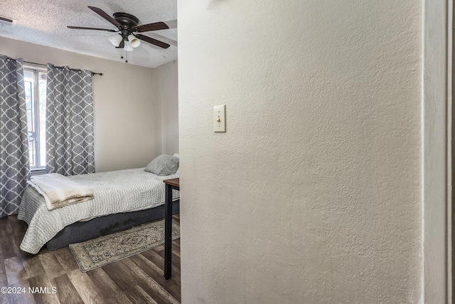 bedroom with ceiling fan, a textured ceiling, and dark hardwood / wood-style flooring