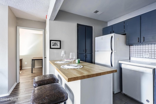 kitchen featuring dishwasher, wooden counters, white refrigerator, blue cabinetry, and a breakfast bar