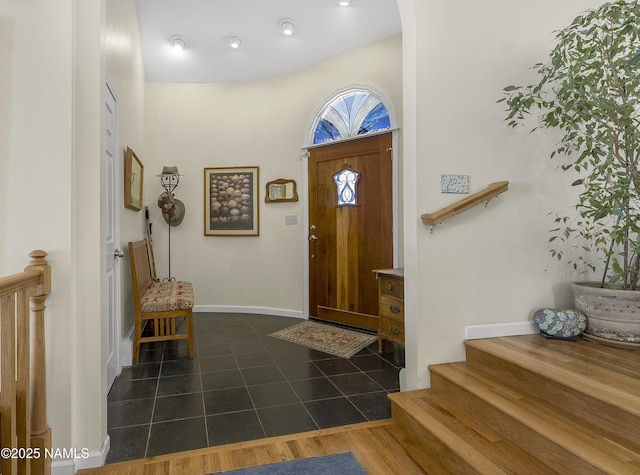 foyer entrance with stairway, baseboards, and dark tile patterned flooring