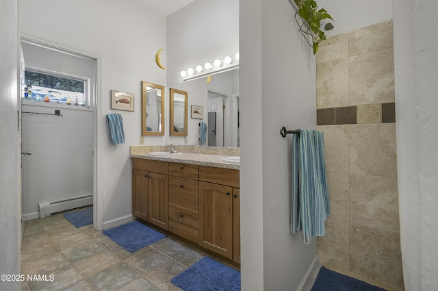 bathroom with baseboards, tiled shower, double vanity, a sink, and a baseboard heating unit