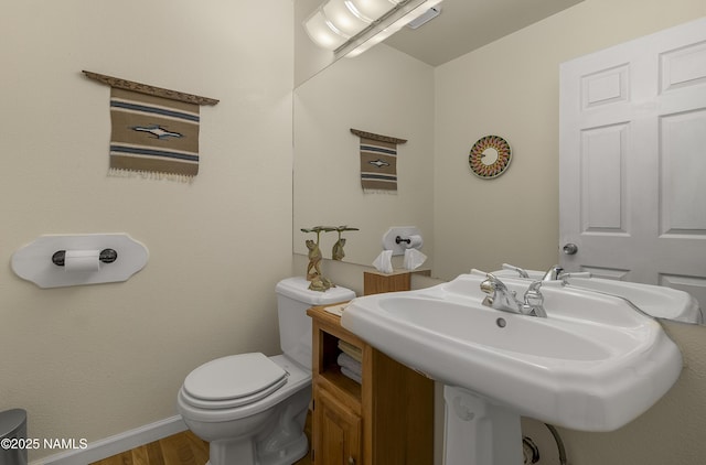 half bathroom with wood finished floors, toilet, baseboards, and a sink