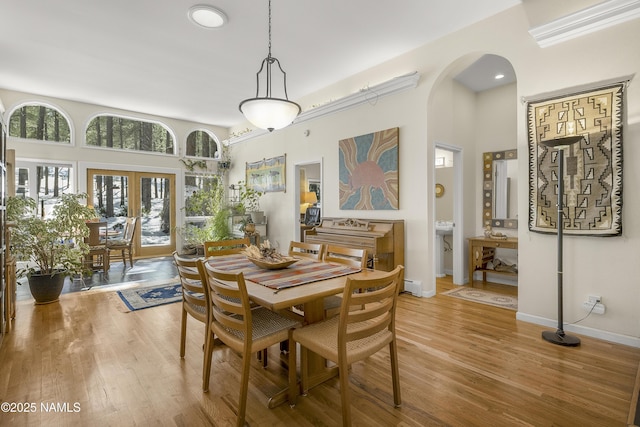 dining room featuring wood finished floors, baseboards, arched walkways, french doors, and a towering ceiling