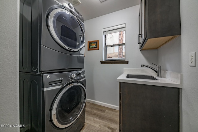 washroom featuring sink, cabinets, light wood-type flooring, and stacked washer / drying machine