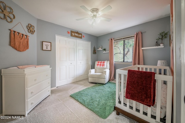 bedroom featuring light carpet, ceiling fan, a crib, and a closet