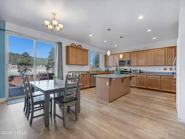 kitchen with light stone counters, recessed lighting, a kitchen island, appliances with stainless steel finishes, and pendant lighting