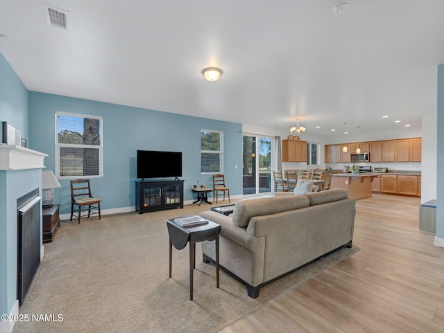 living room with a fireplace, visible vents, an inviting chandelier, light wood-style floors, and baseboards