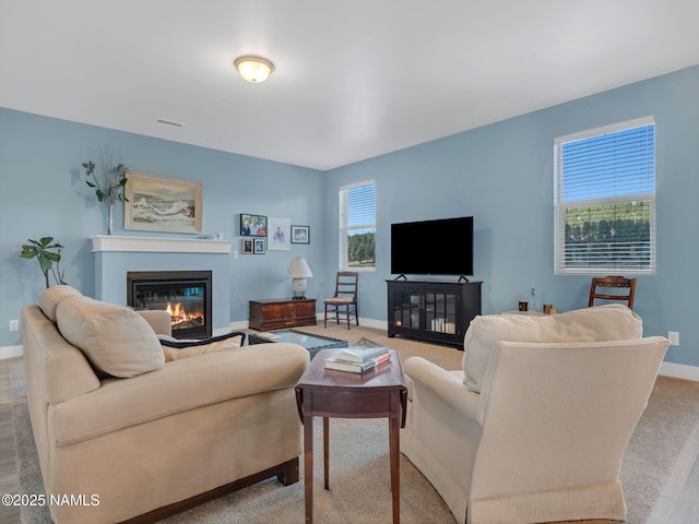 living room featuring carpet floors, visible vents, baseboards, and a glass covered fireplace