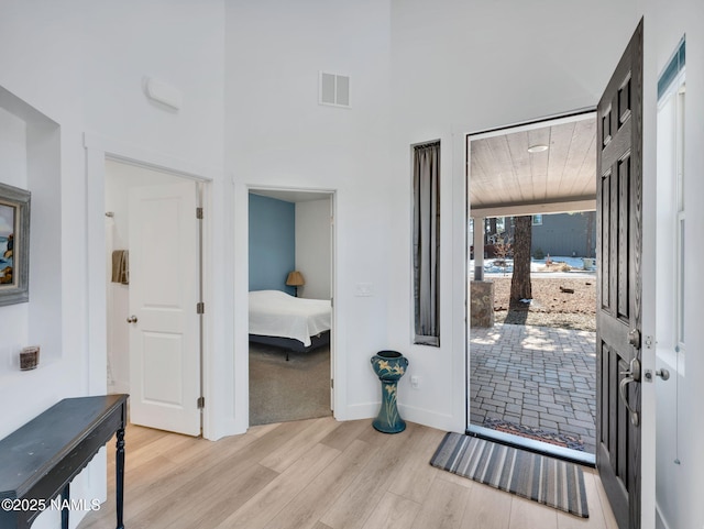 entryway with a high ceiling, light wood-type flooring, visible vents, and baseboards