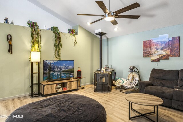 living room featuring ceiling fan, a wood stove, light hardwood / wood-style flooring, and lofted ceiling