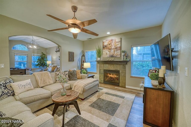 living room featuring light wood-type flooring, ceiling fan with notable chandelier, a healthy amount of sunlight, and a tile fireplace