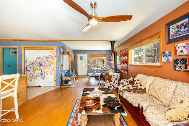 living area with a ceiling fan, wood finished floors, and a wood stove