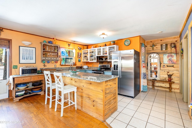 kitchen with open shelves, stone countertops, a sink, stainless steel appliances, and a kitchen bar