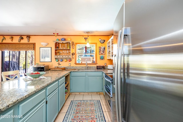 kitchen featuring a peninsula, light tile patterned flooring, a sink, appliances with stainless steel finishes, and decorative light fixtures