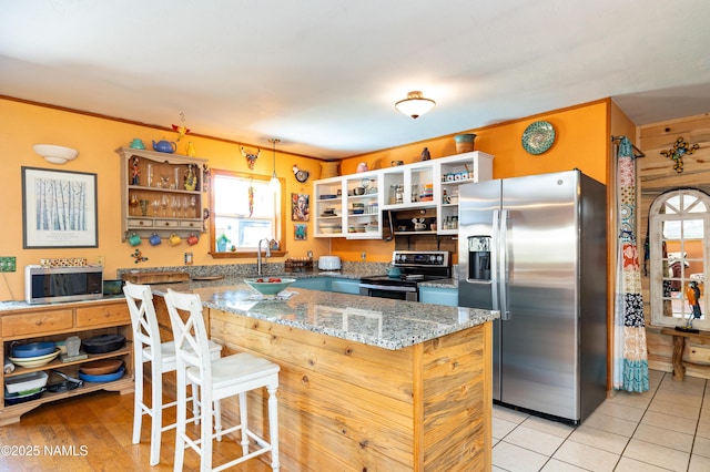 kitchen with a sink, appliances with stainless steel finishes, a kitchen breakfast bar, and open shelves