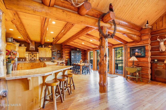 kitchen featuring a kitchen bar, rustic walls, wall chimney range hood, vaulted ceiling with beams, and kitchen peninsula