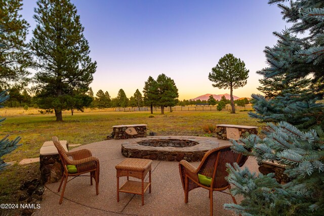 patio terrace at dusk featuring a mountain view, an outdoor fire pit, and a rural view