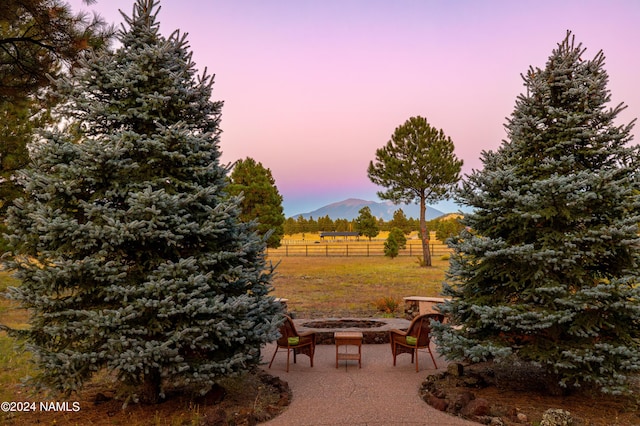 yard at dusk with a mountain view, a patio, a rural view, and a fire pit